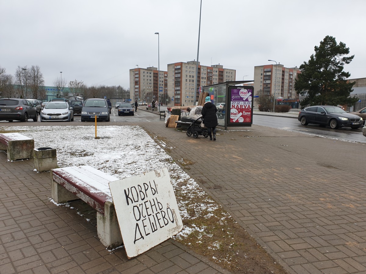 Linnaväljak, taamal kõrged kortermajad, esiplaanil käsitsi kirjutatud venekeelne plakat. 