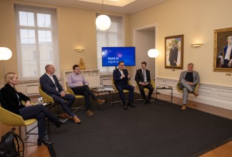 Kuus meest istuvad toolidel, taustal ekraanil kiri Eesti.ai